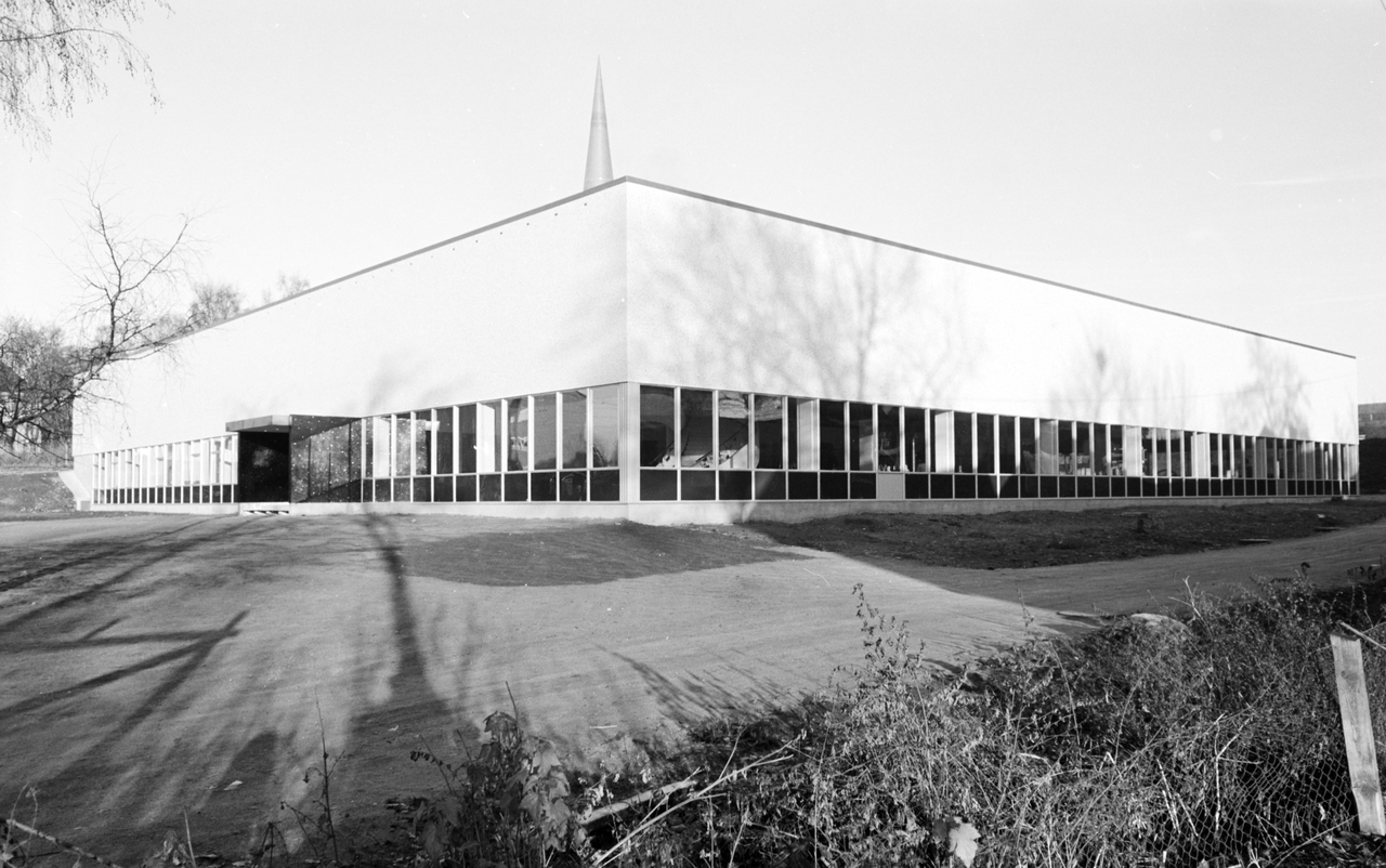 Fasaden på nybgget. Et sammenhengende bånd av vinduer i første etasje. Kjegleformet tårn/markør på taket.