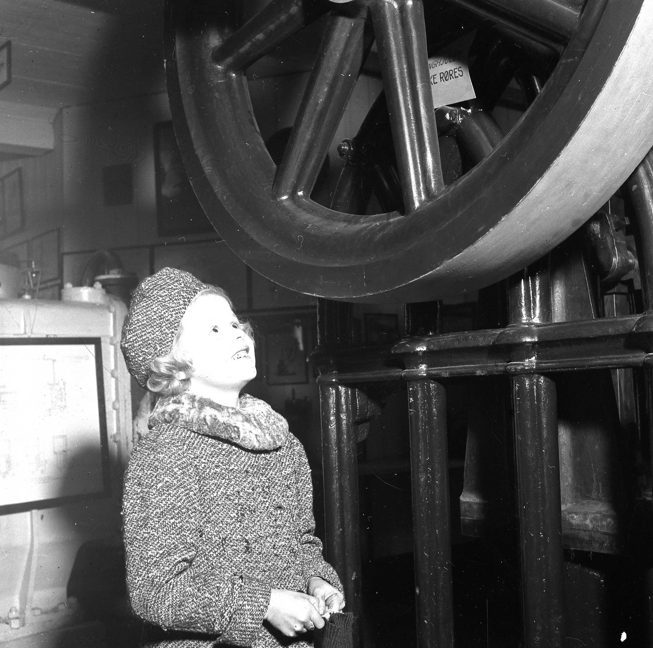 Liten pike ser opp på en gammel maskin med stort svinghjul