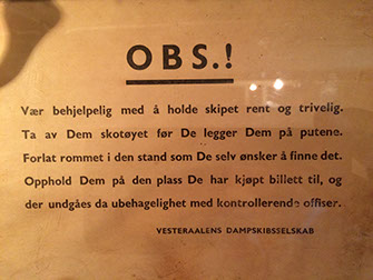 Gulnet plakat med teksten: OBS.! Vær behjelpelig med å holde skipet rent og trivelig. Ta av Dem skotøyet for De legger Dem på putene. Forlat rommet i den stand som De selv ønsker å finne det. Opphold Dem på den plass De har kjøpt billett til, og der undgåes da ubehagelighet med kontrollerende offiser. Undertegnet: VESTERAALENS DAMPSKIBSSELSKAB